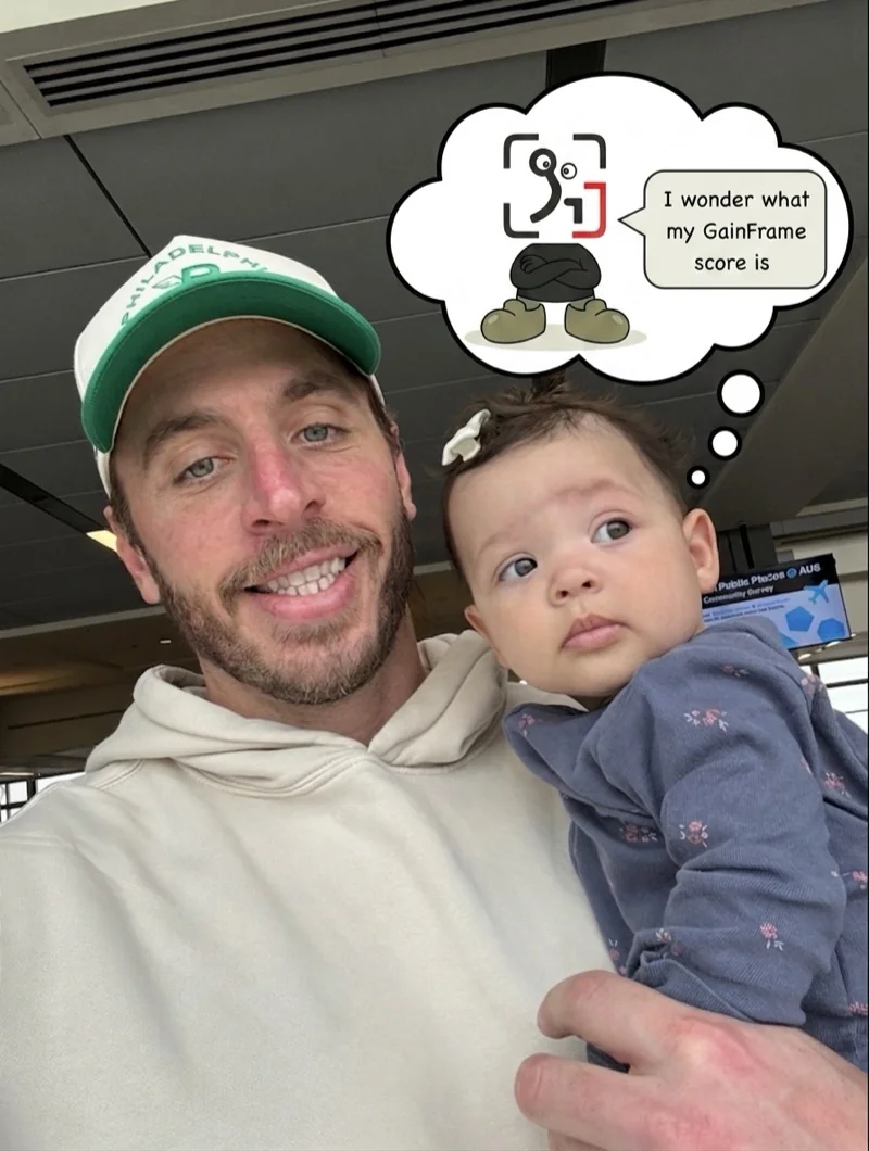 Michael Rode, founder of GainFrame, holding his 5-month-old daughter at the airport — with a thought bubble showing the GainFrame Guy mascot wondering 'I wonder what my GainFrame score is'
